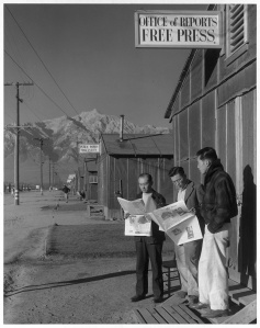 Fig 13: Adams, Ansel 1943: Roy Takeno, editor, and group reading paper in front of office, Manzanar Relocation Center, California